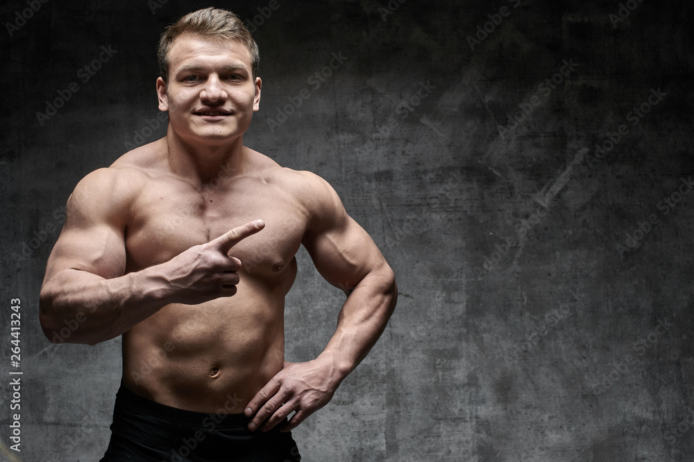 Sexy muscular bodybuilder shows index finger to the side, advertising something. Athletic pumped male body with copy space for your product Sexy muscular bodybuilder shows index finger to the side, advertising something. Athletic pumped male body with copy space for your product