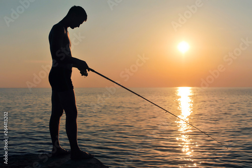 Silhouette of a fisherman at sunset on the background of the sea and sky