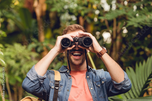 adult happy traveler looking through binoculars in tropical green forest