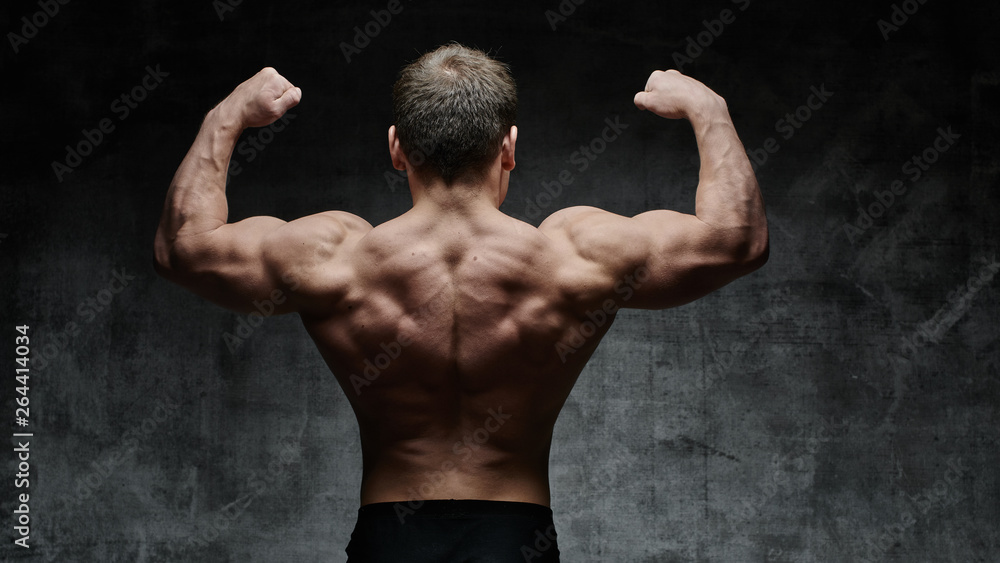 Sexy bodybuilder man posing from the back on dark background. Handsome pumped male body isolated with free space for advertising