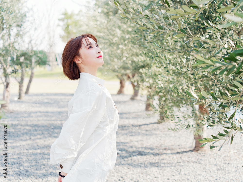 Portrait of a beautiful Chinese woman in white shirt stand in orchard in sunny day, looking upwards with hand behind herself, elegant girl. Portrait of a beautiful Chinese woman in white shirt stand in orchard in sunny day, looking upwards with hand behind herself, elegant girl.