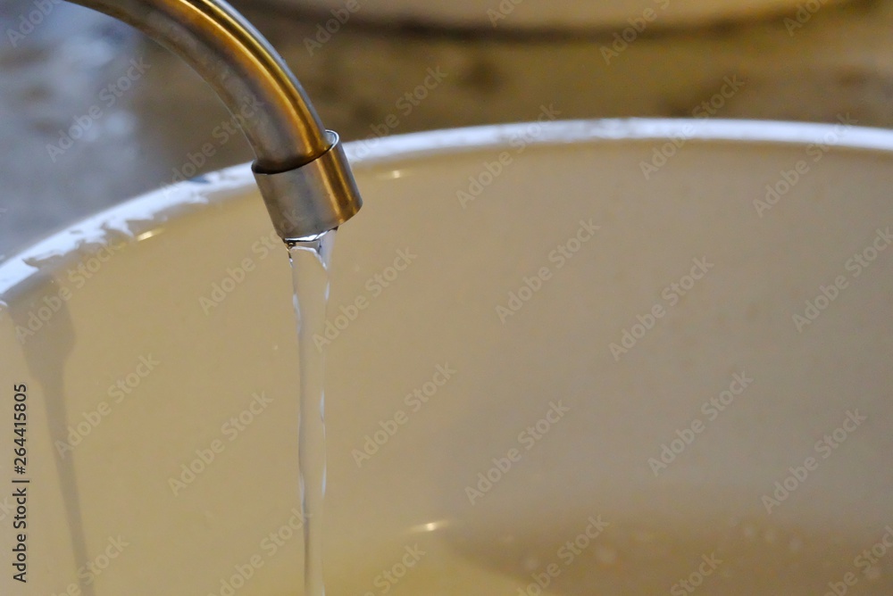 Water flowing from a steel faucet in a bathroom at night with blur a white sink for saving water concept Water flowing from a steel faucet in a bathroom at night with blur a white sink for saving water concept