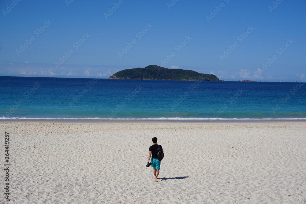 Man walking on the secluded beach in paradise with fine white sand towards the ocean seaside barefoot relaxation holiday