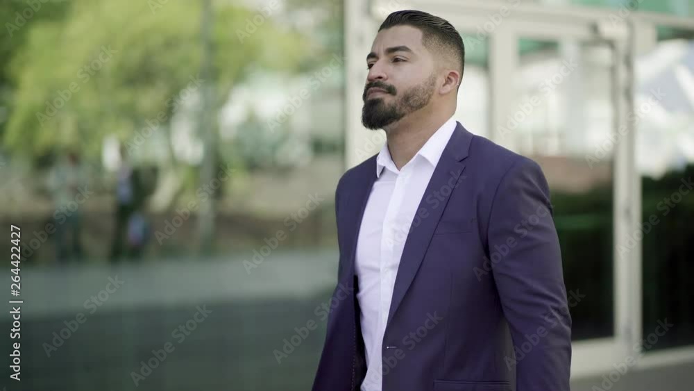 Confident businessman with laptop on street. Tracking shot of serious bearded businessman holding laptop computer and walking near modern building. Confidence concept Confident businessman with laptop on street. Tracking shot of serious bearded businessman holding laptop computer and walking near modern building. Confidence concept