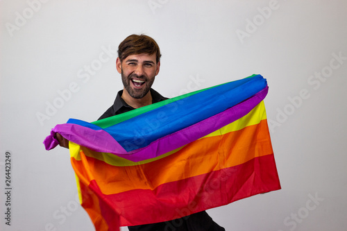 Portrait of handsome young man with gay pride movement LGBT Rainbow flag and brown hair looking seductive  their back facing the camera and looking at the camera. Isolated on white background.