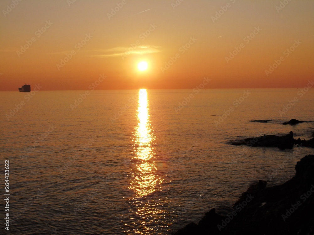 Fototapeta premium Genova, Italy - 03/15/2019: An amazing caption of the sunset in spring days over the sea of Genova with beautiful red and blue sky, some amazing clouds in the background and old rocks over the sea.