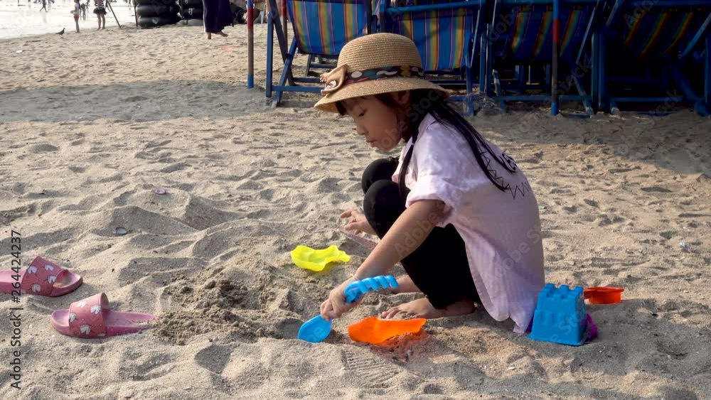 Asian child girls wearing hats, playing sand piles on the beach on family holidays Asian child girls wearing hats, playing sand piles on the beach on family holidays
