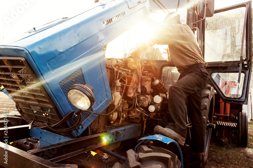 Farmer mechanic repairing blue tractor engine. Repair agricultural technology at sunset.