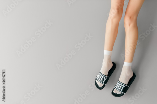 Beautiful female legs in white mesh teen socks wearing fashionable rubber slippers with inscroption why noton gray background. Elegant stylish trendy leg wear . Voguish footwear for fashionable ladies photo