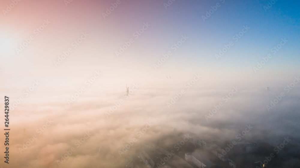 The city is covered with thick fog and protruding from it where neither where high-rise buildings