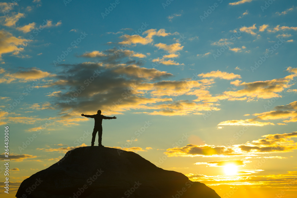 Silhouette of a man at the top of the mountain, against the backdrop of the sunset. Happy, hands raised, winner