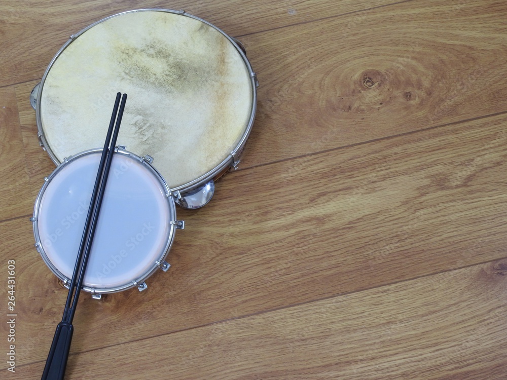 Fototapeta premium Two Brazilian percussion musical instruments: pandeiro (tambourine) and tamborim with drumstick on a wooden surface. The instruments are widely used to accompany samba, a popular Brazilian rhythm.