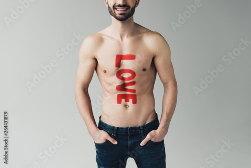 Cropped view of shirtless man with inscription on body standing with hands in pockets on grey