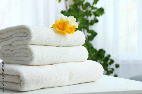 Stack of fresh towels with flowers on table indoors. Space for text