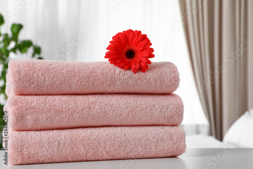 Stack of fresh towels with flower on table in bedroom. Space for text