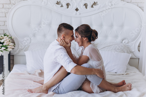 Photo session of the guy and the girl in a cozy white bedroom.