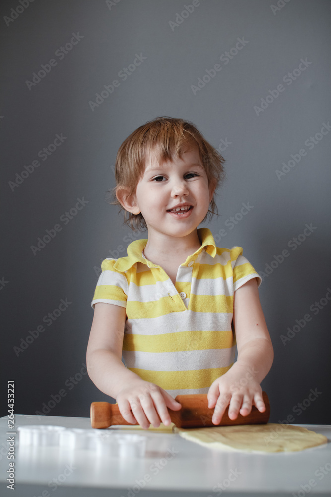 Little cute girl making shortbread. Rolls out the dough with a rolling pin on a white table. The preparation of the dessert Little cute girl making shortbread. Rolls out the dough with a rolling pin on a white table. The preparation of the dessert