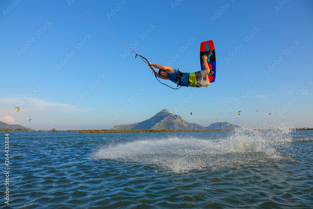 Athletic male kitesurfer jumps in the air and sprays the glassy ocean water. Athletic male kitesurfer jumps in the air and sprays the glassy ocean water.