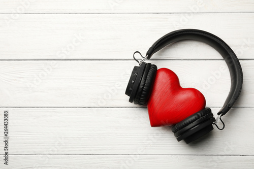 Decorative heart with modern headphones on wooden background, top view. Space for text