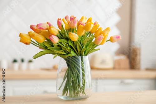 Close-up of a bouquet of fresh spring yellow tulips in a large transparent glass vase in a photo studio against the background of beautiful kitchen. Concept photography for a flower shop