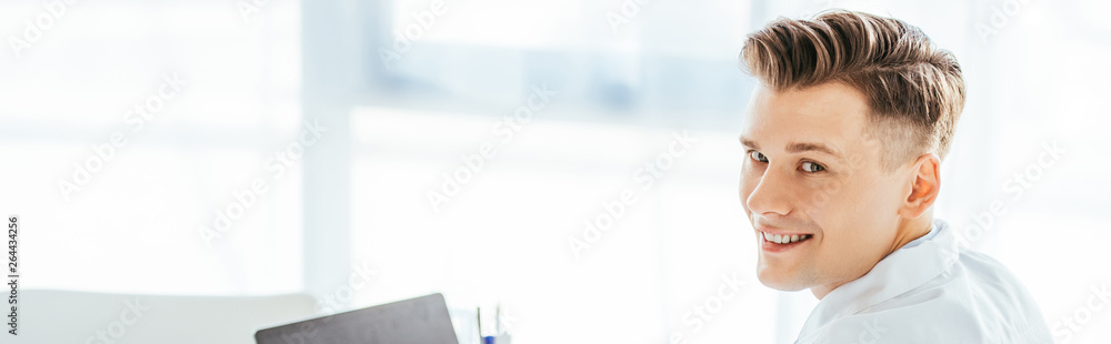 Obraz premium panoramic shot of cheerful and handsome doctor looking at camera