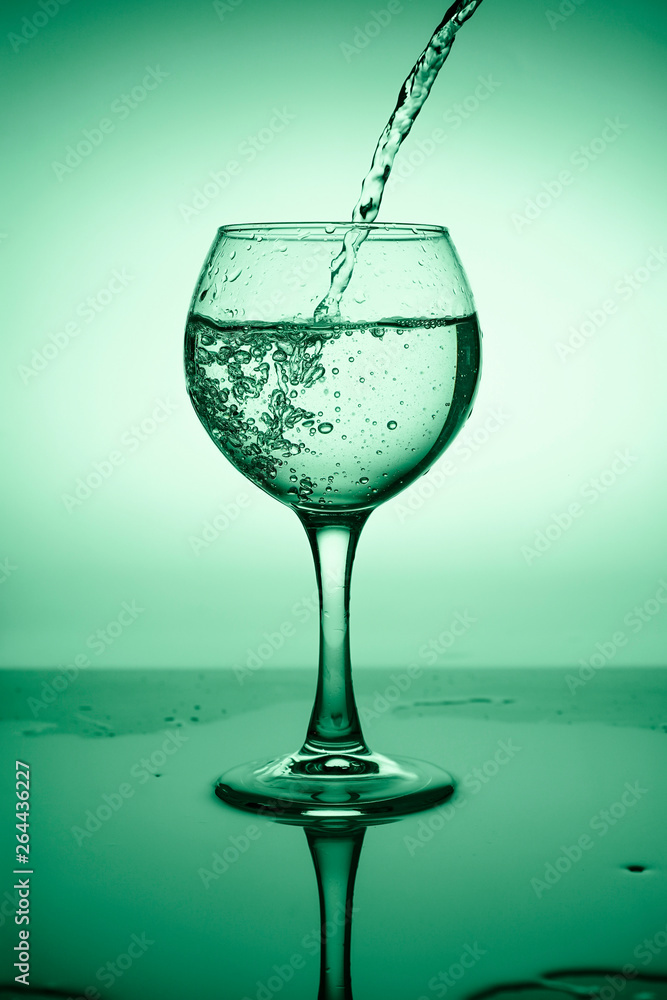 Wine glass with flowing water (white wine) on a background of green gradient Wine glass with flowing water (white wine) on a background of green gradient