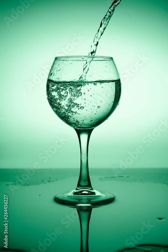 Wine glass with flowing water (white wine) on a background of green gradient