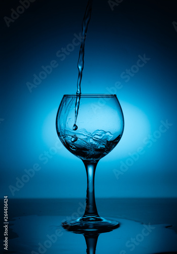 Wine glass with flowing white wine (water) on a blue gradient background