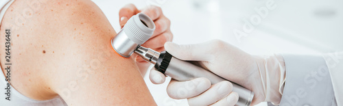 panoramic shot of dermatologist in latex glove holding dermatoscope while examining patient photo