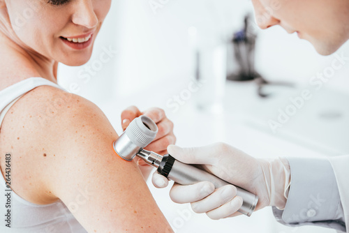 cropped view of dermatologist holding dermatoscope while examining cheerful woman with skin disease