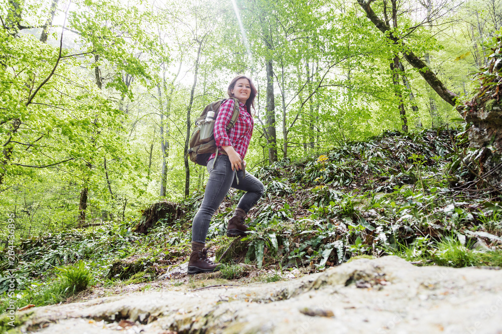 Hiker woman with backpack walking on path in summer forest