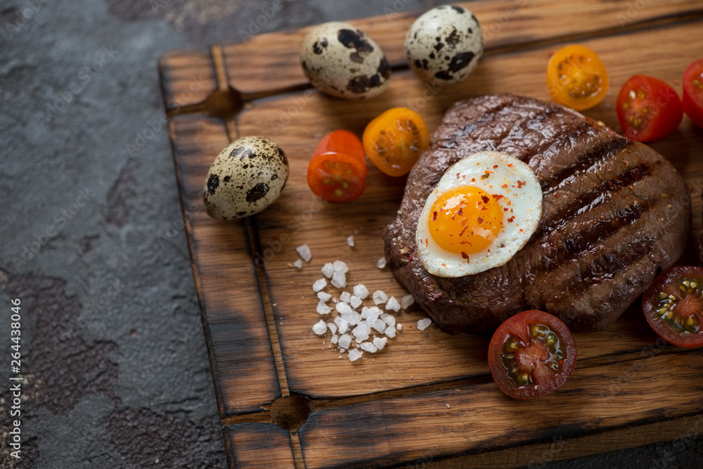 Close-up of grilled marbled beefsteak with fried quail egg and cherry tomatoes, elevated view, horizontal shot Close-up of grilled marbled beefsteak with fried quail egg and cherry tomatoes, elevated view, horizontal shot