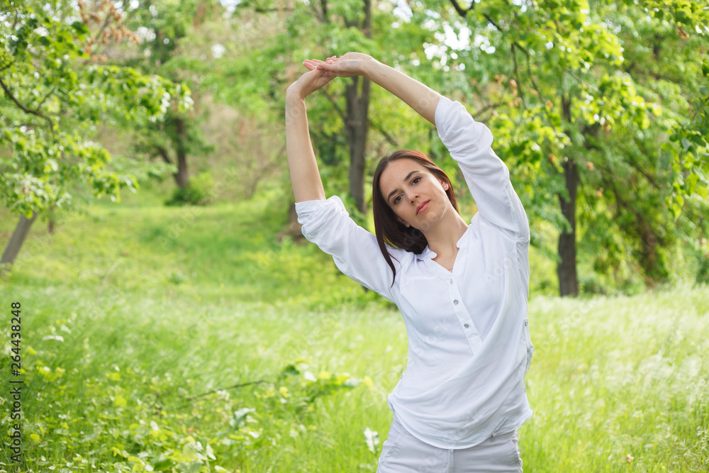 Young woman enjoying nature in a park. Beautiful Girlin white with arms up. Outdoor image. Young woman enjoying nature in a park. Beautiful Girlin white with arms up. Outdoor image.
