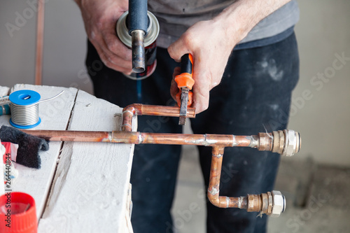 Closeup professional master plumber hands soldering copper pipes gas burner. Concept installation, plumbing replacement, solder flux paste, pipeline repair, professional master, pipe leakage