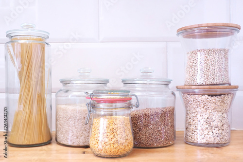 Glass jars of food and olive oil stand on.countertop on the background of white ceramic tiles in the form of bricks...