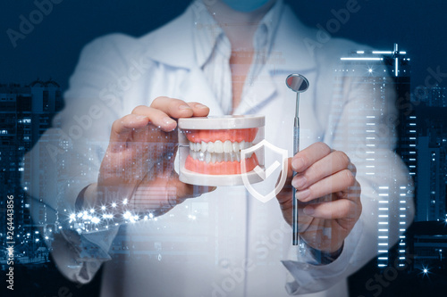 A dentist showing a denture model and a dental mirror with quality sign in front of.