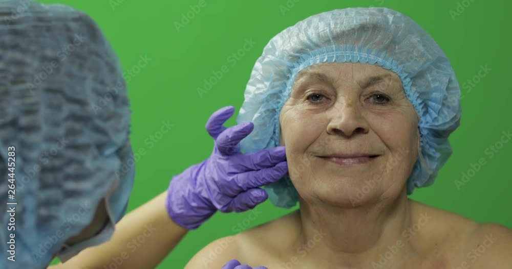Smiling elderly female in protective hat. Plastic surgeon checking woman face