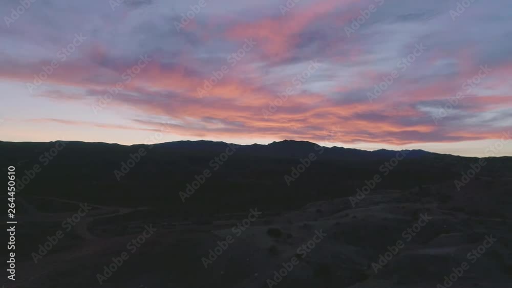 Drone shot flying up and over brush and winding desert roads toward mountains and colorful sunset. Springtime. Drone shot flying up and over brush and winding desert roads toward mountains and colorful sunset. Springtime.