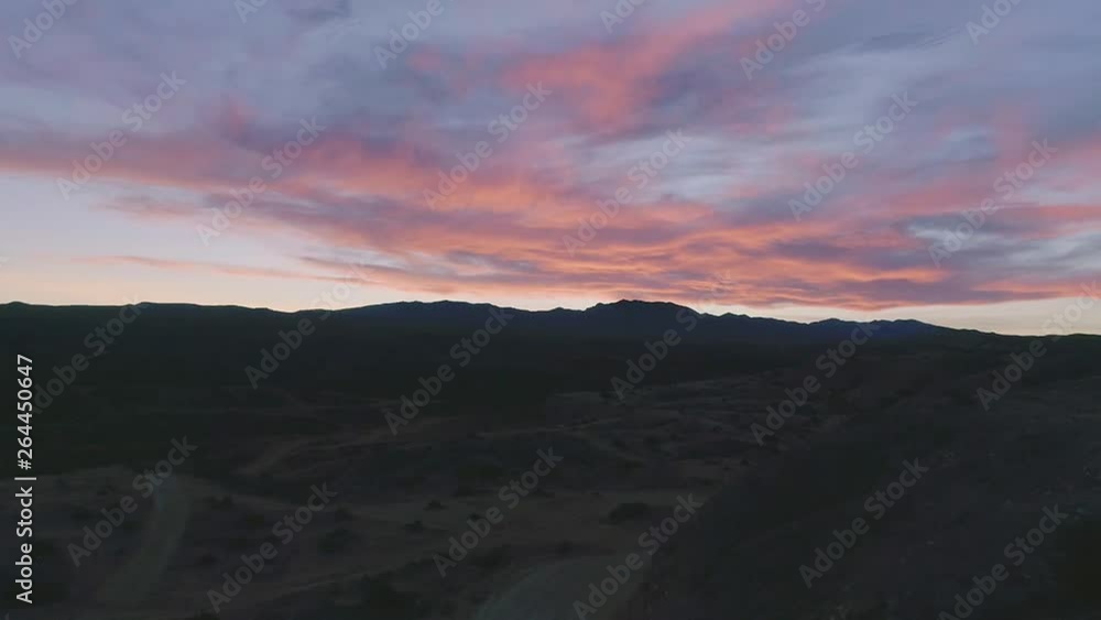Drone shot flying up and over brush and winding desert roads toward mountains and colorful sunset. Springtime. Drone shot flying up and over brush and winding desert roads toward mountains and colorful sunset. Springtime.