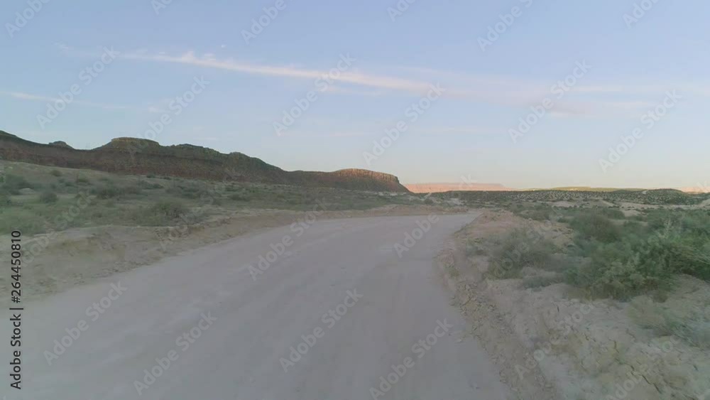 Aerial shot flying down along and towards desert road at sunset during early spring. Cliffs in distance. Aerial shot flying down along and towards desert road at sunset during early spring. Cliffs in distance.