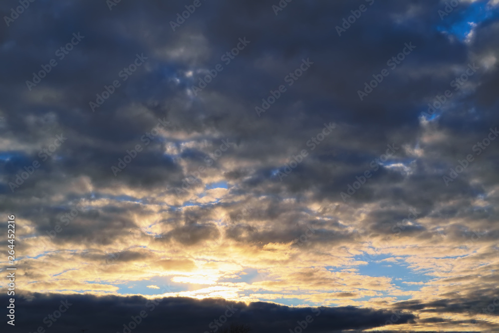 Fototapeta premium Blue sky with gold clouds - dramatic sunset, beautiful natural background. Setting sun illuminates the clouds.