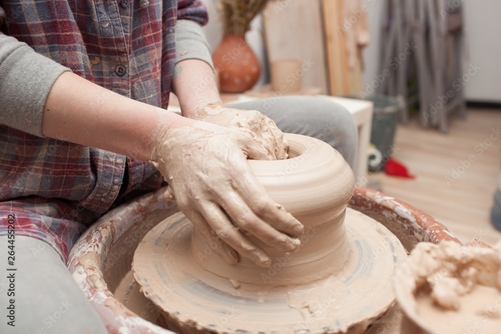 Potter working on potters wheel making ceramic pot from clay in pottery workshop