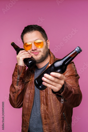 Photo of brunet man in orange glasses and leather jacket with two bottles in hands