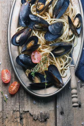 Spaghetti with mussels, tomatoes in spicy sauce in the original plate on the old wooden table. Clams Mytilus closeup. Italian pasta. A dish for a romantic dinner. View from above.