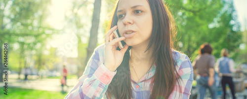 A woman sitting on a bench in the Park and talking on the phone. Brunette in a shirt calls on a smartphone