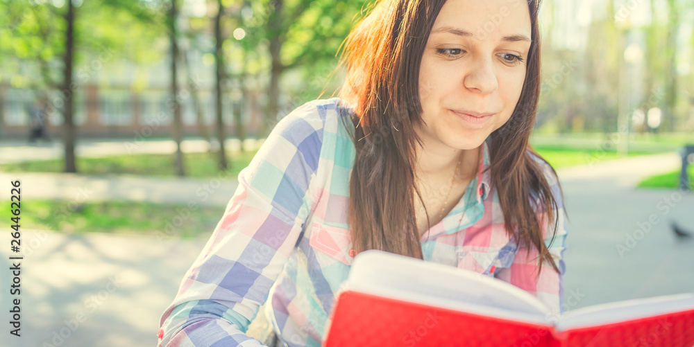Woman with a book in his hands in the Park. Female, student is reading an interesting book sitting on the bench in the park Woman with a book in his hands in the Park. Female, student is reading an interesting book sitting on the bench in the park