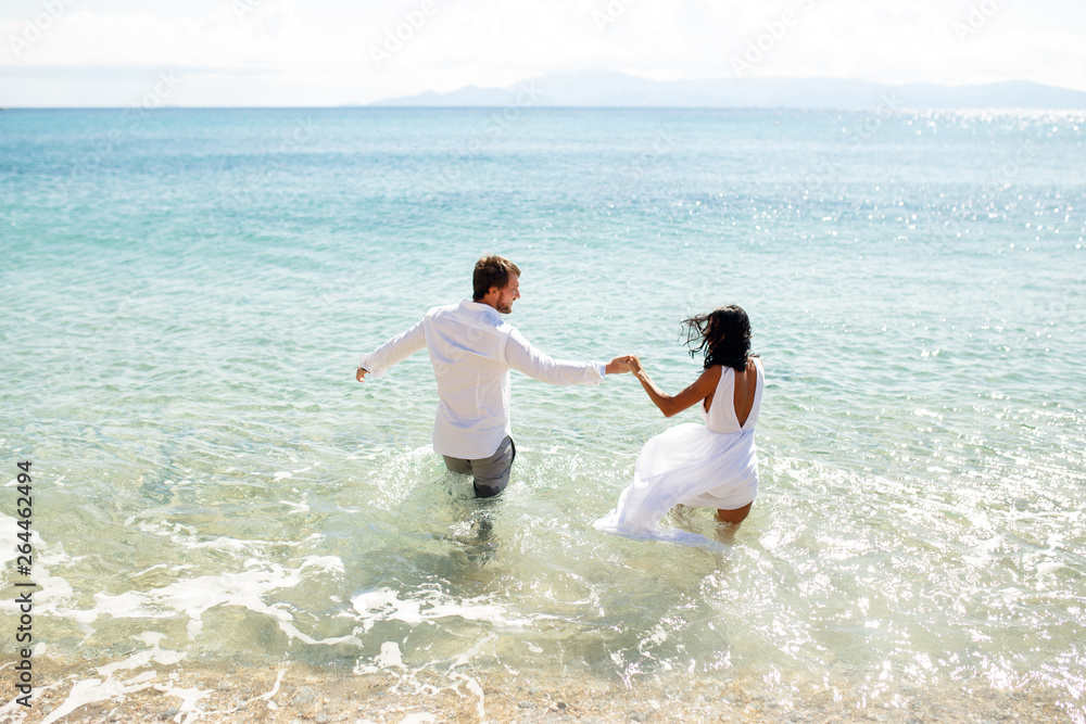 Back view of two young person newlyweds enter in water in clothing, enjoy in holiday, summer time, sea in Greece. Back view of two young person newlyweds enter in water in clothing, enjoy in holiday, summer time, sea in Greece.