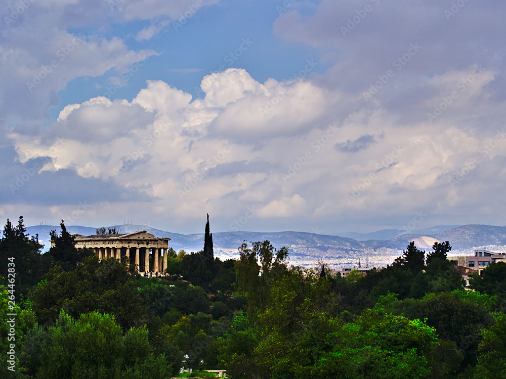 Temple of Hephaestus in Athens, Greece. Landscape with olive, cypress and other trees cloudy sky, bright light, and ancient greek temple.
