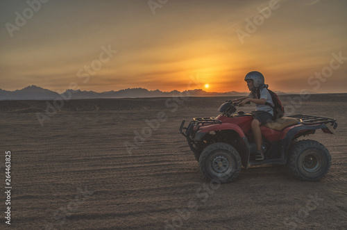 boy drives a quad bike through the desert at sunset