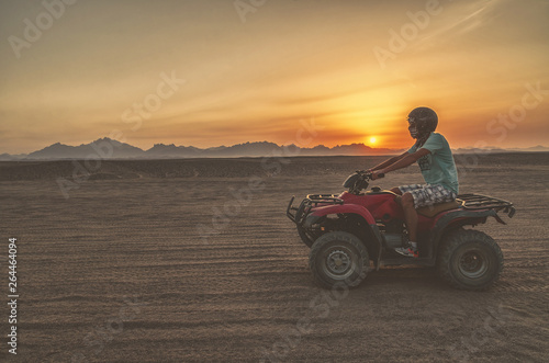 A man travels on an quad bike in the desert at sunset